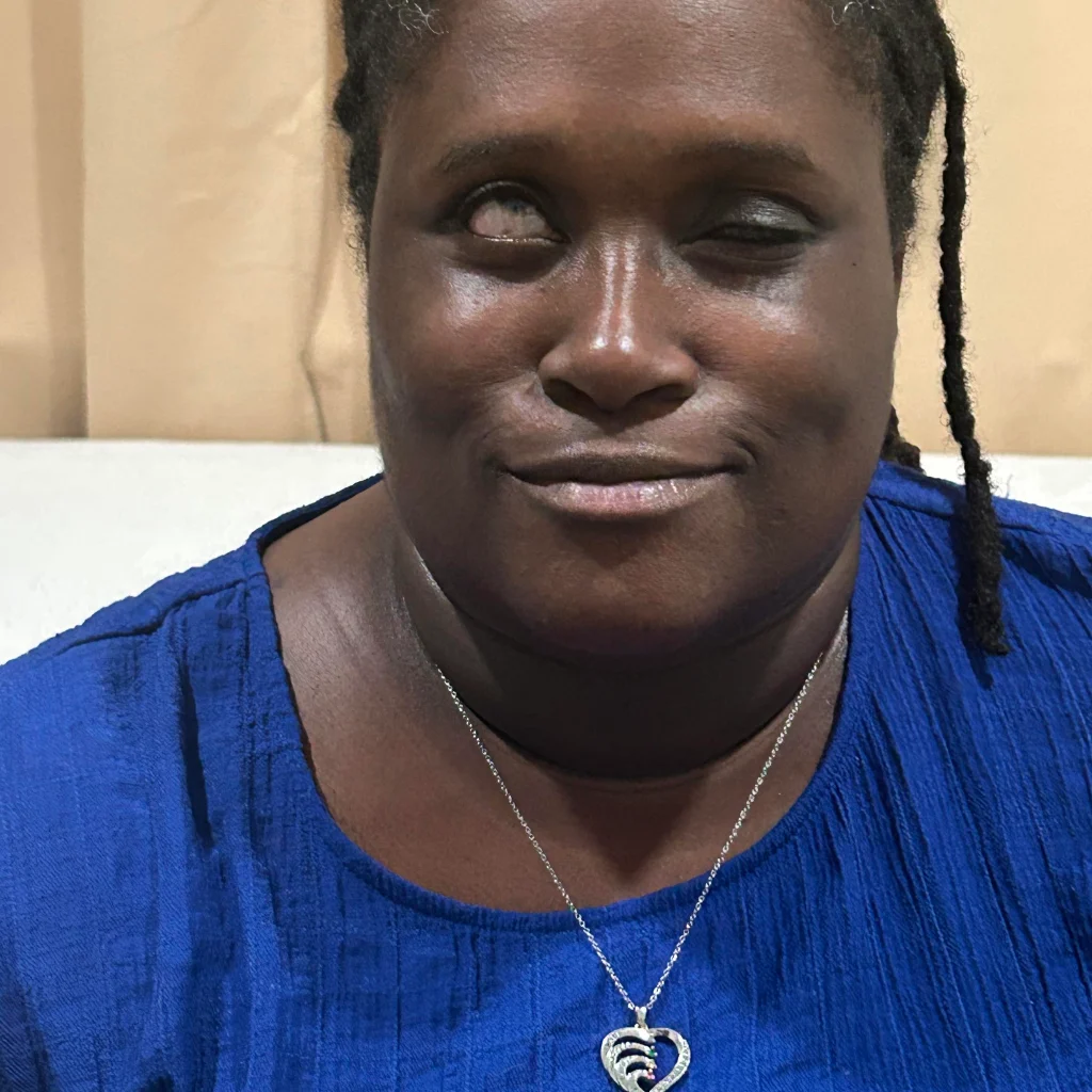 Portrait of a woman smiling. She is wearing a blue shirt and necklace.